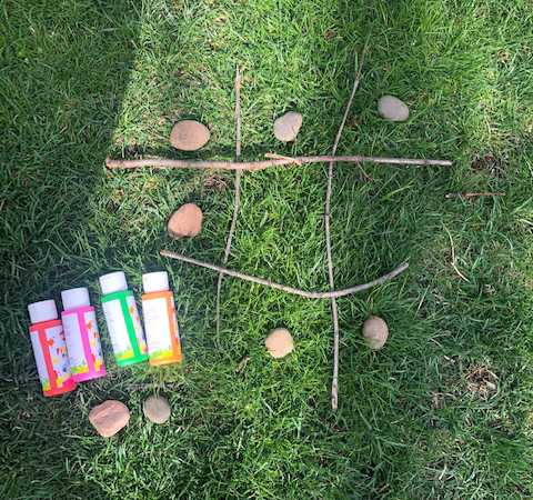 Example of rock tic tac toe with the use of branches to make the game board.  Shows paint bottles that could be used to paint the rocks to make the game pieces.